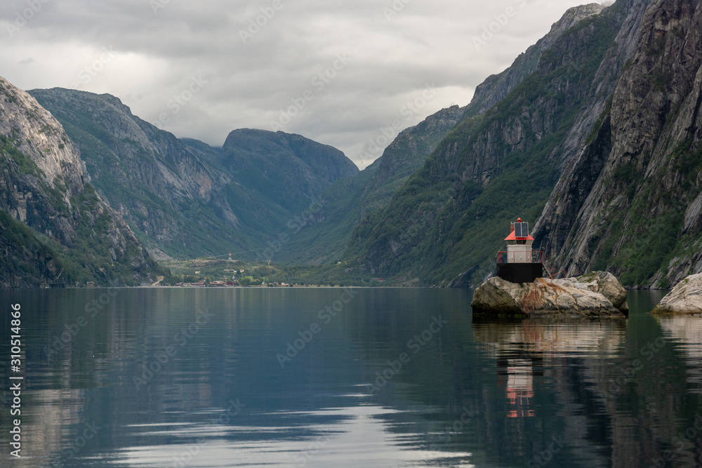 Small idyllic lighthouse surrounded by mountains in the majestic Lysefjord in Norway. Seen from the seaside