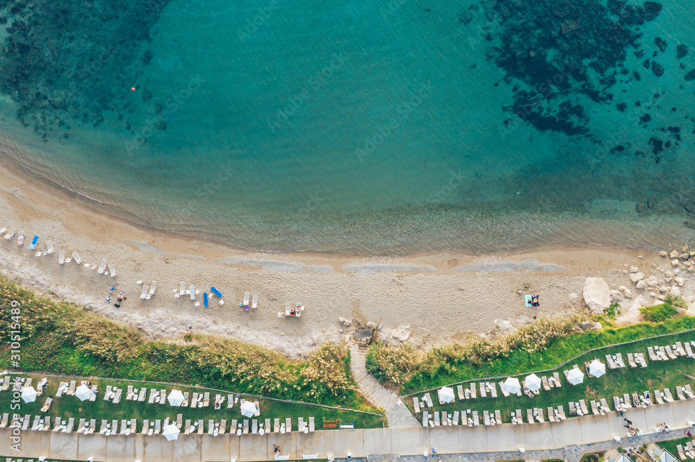 Aerial view of Cyprus beach with people on sunbeds and umbrellas and sea water surface.
