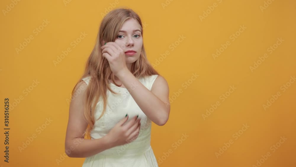 Attractive blonde young woman over isolated orange background wearing white shirt hugging herself, keeping hands crossed. Lifestyle concept Attractive blonde young woman over isolated orange background wearing white shirt hugging herself, keeping hands crossed. Lifestyle concept