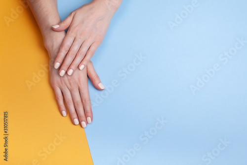 Beautiful female hands with a classic matte manicure on a blue-yellow background. Place for your text.