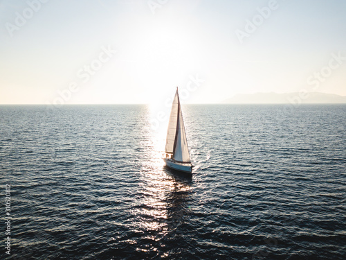 Foto Silhouette of a yacht under sail opposite the reflection of the sun from the wat