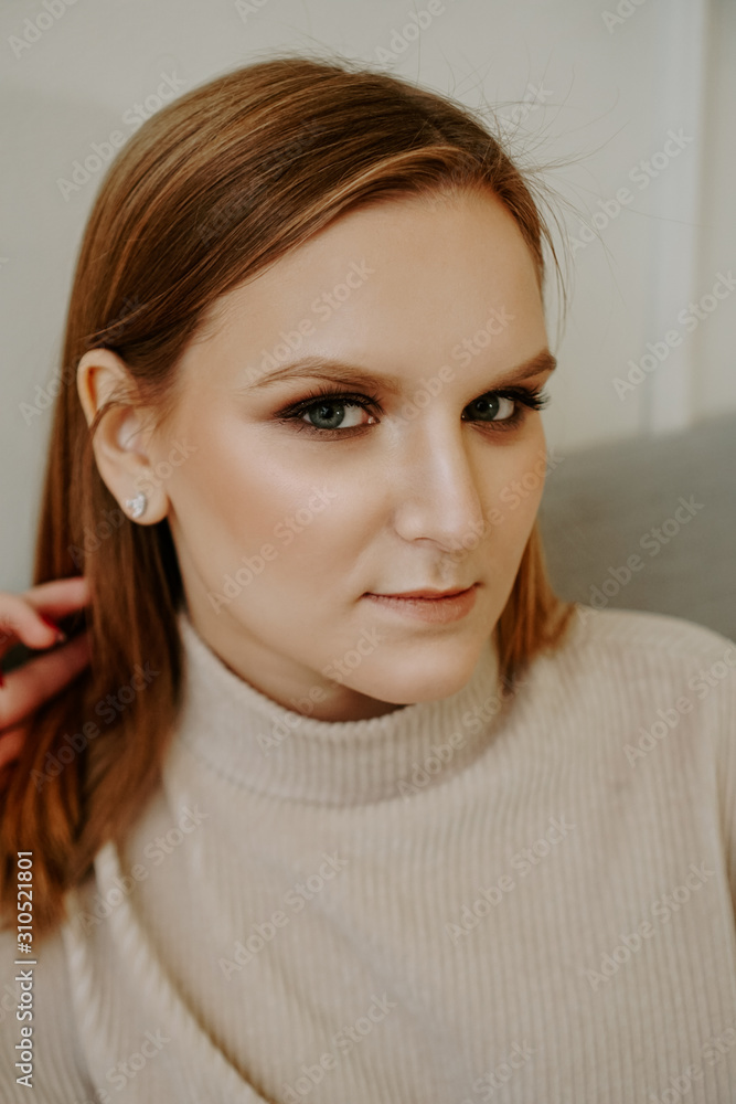 Naklejka premium Portrait of Woman with bright makeup and strict facial features dressed in beige sweater sitting on bed