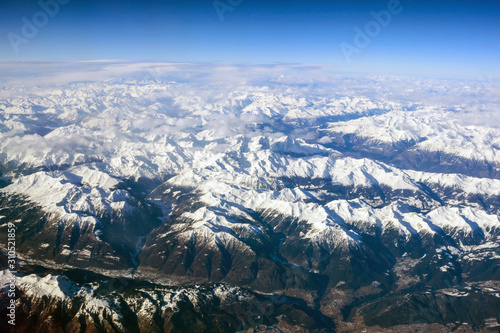 Winter landscape. Beautiful Alps mountains with peaks covered in snow. Photo from the porthole of an airplane.