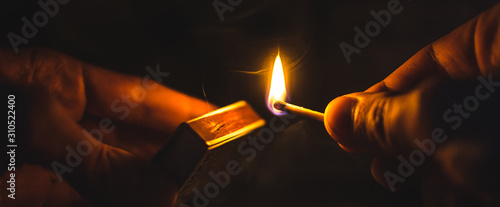 A match lit in the dark in hands with a matchbox photo