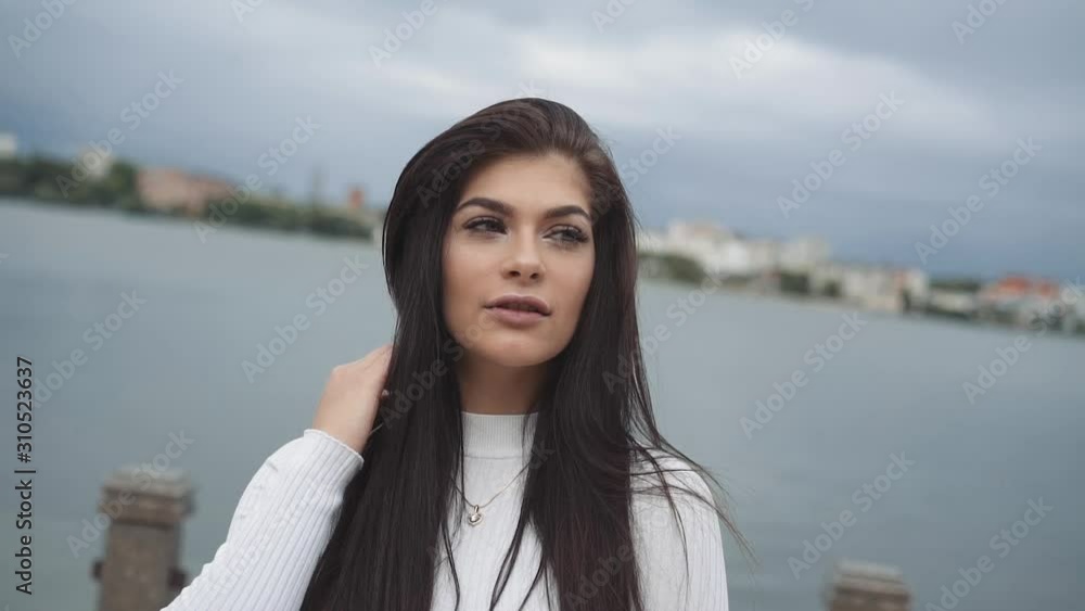 Pretty brunette poses, touches her long hair at camera on lake background Pretty brunette poses, touches her long hair at camera on lake background