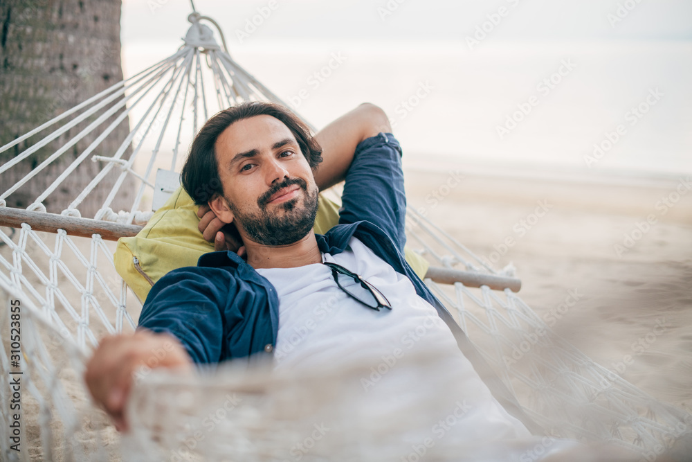 A man enjoys calm, lies in a hammock on the background of the ocean and sunset.