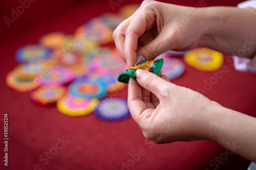 Woman hands working on handicrafts, small round embroidery, full of colors, shown on a red background