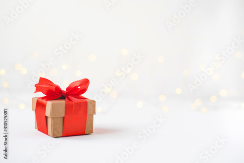 Wallpaper Mural Gift box with a red bow on a background of blurred lights garland. Christmas background. Torontodigital.ca