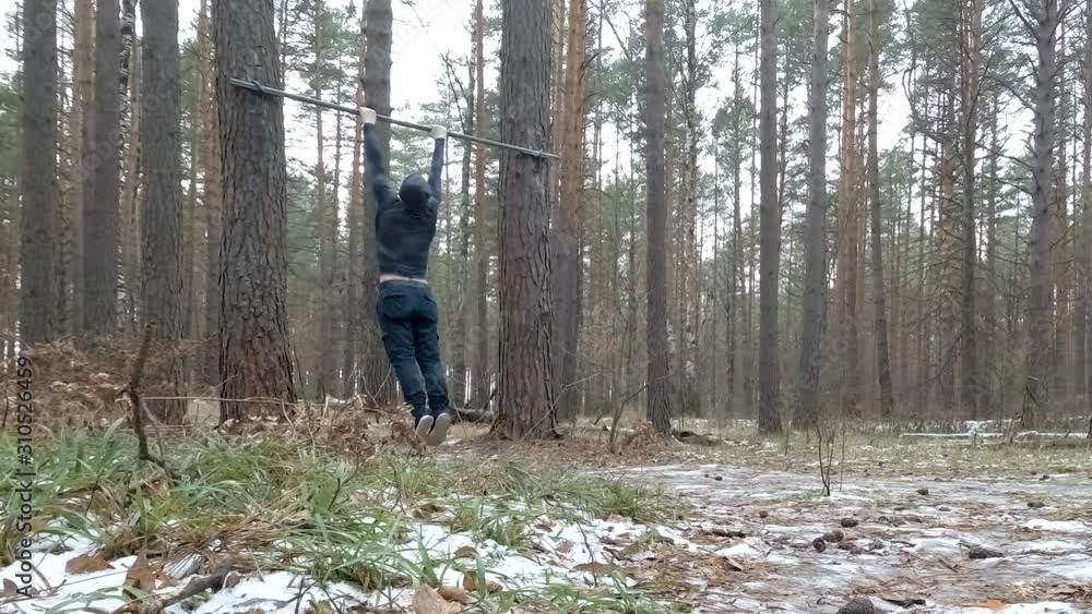 Young Athletic Man Performs Pullups in forest Young Athletic Man Performs Pullups in forest