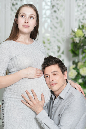 Portrait of happy pregnant woman with husband at home. Man with head on belly of wife