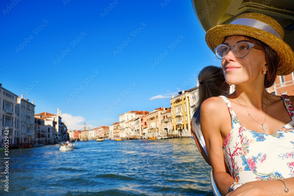 Tourist woman in hat travel by vaporetto on Grand Canal on vacation in Venice, Italy. Young girl in romantic dress smiling, looking on Grand Canal great view, traveling during holidays in Europe.
