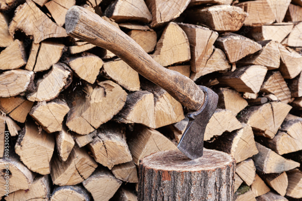 Dry oak firewood stacked in a pile, chopped wood for winter heating of the fireplace. An ax and a deck for chopping wood. Natural wood background. Dry oak firewood stacked in a pile, chopped wood for winter heating of the fireplace. An ax and a deck for chopping wood. Natural wood background.