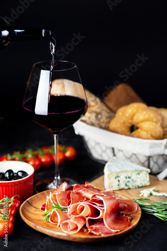 Wine snack on a wooden board. Red wine, cheese, jamon, prosciutto, with salami and olives on a black background. freshly baked bread with cheese and wine snacks. Delicious red wine party snacks