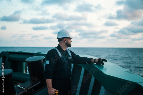 Marine Deck Officer or Chief mate on deck of offshore vessel or ship , wearing PPE personal protective equipment - helmet, coverall. He holds VHF walkie-talkie radio in hands.