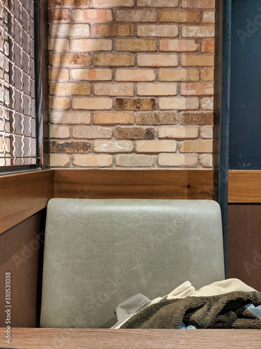 View of one side of a small, padded booth inside a brick restaurant and bar, a warm jacket slung in the seat behind a wooden table top