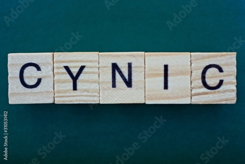 word cynic made from wooden gray letters lies on a green background