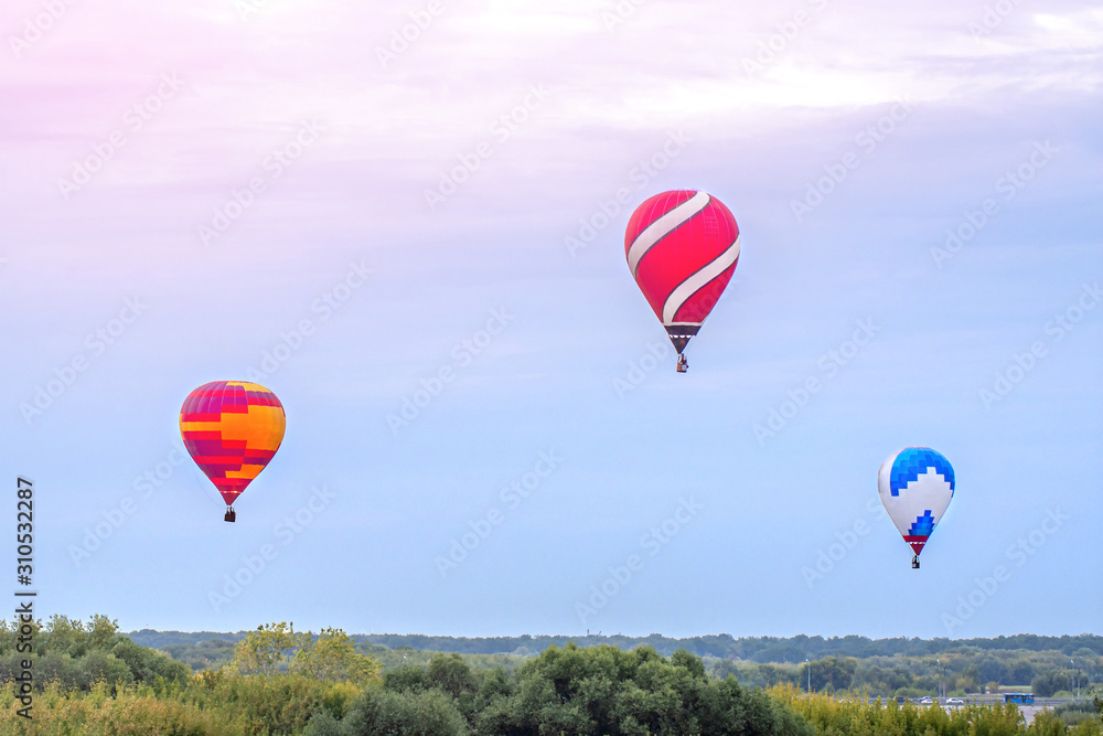 three colorful hot air balloons fly in the blue sky over the green meadow