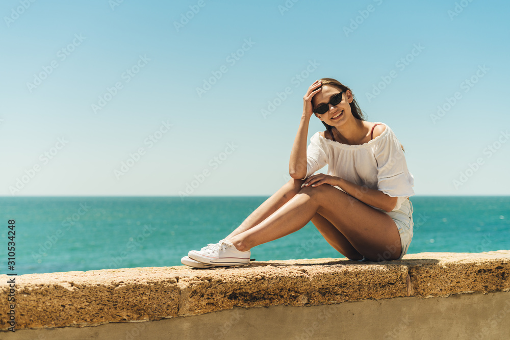the girl climbed onto the parapet and sits on it, resting her elbows on her knees, behind the sea