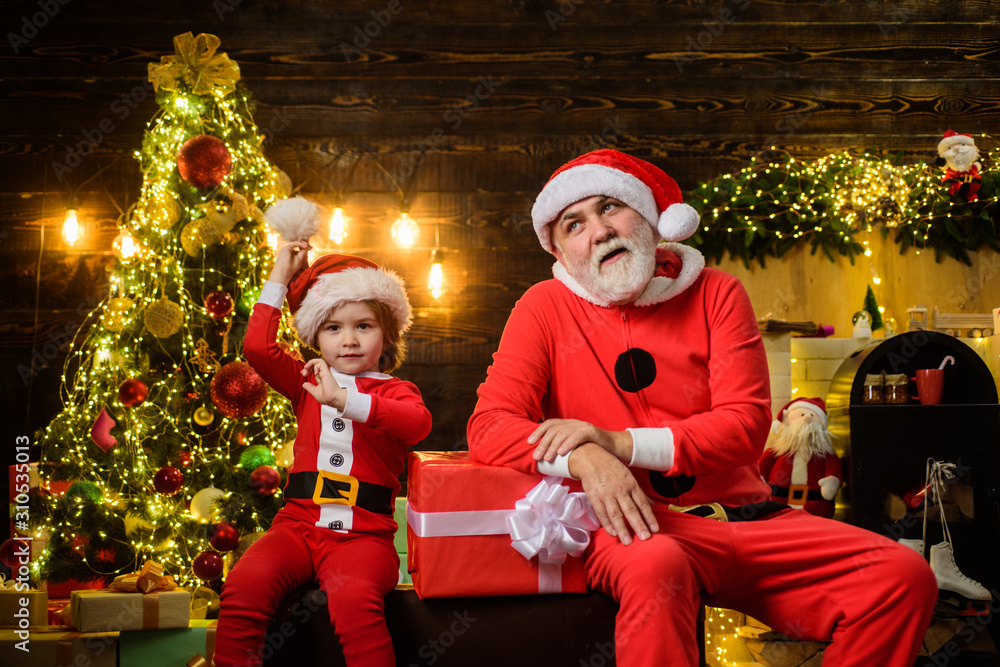 Happy holidays. Smiling little child boy in santa costume with Santa Claus. Christmas gift. Family holiday concept. Santa Claus man and little Santa boy at home. Merry Christmas. Christmas decoration. Happy holidays. Smiling little child boy in santa costume with Santa Claus. Christmas gift. Family holiday concept. Santa Claus man and little Santa boy at home. Merry Christmas. Christmas decoration.