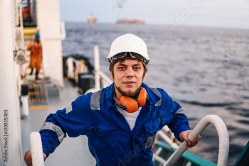 Marine Deck Officer or Chief mate seaman on deck of offshore vessel or ship , wearing PPE personal protective equipment - helmet, coverall. he climbs the ladder