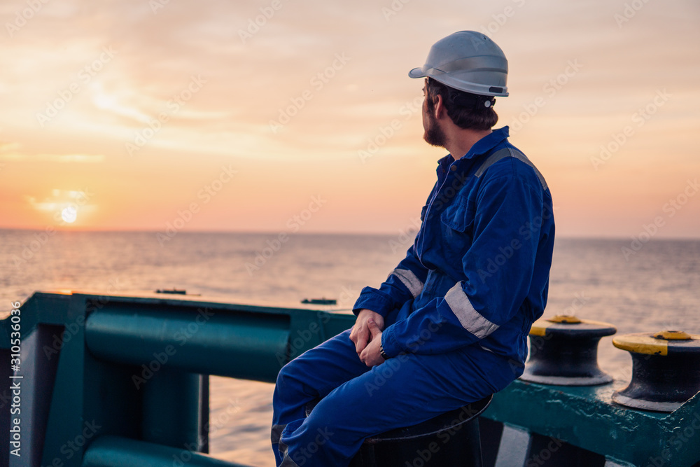 Marine Deck Officer or Chief mate on deck of offshore vessel or ship , wearing PPE personal protective equipment - helmet, coverall. Sunset light