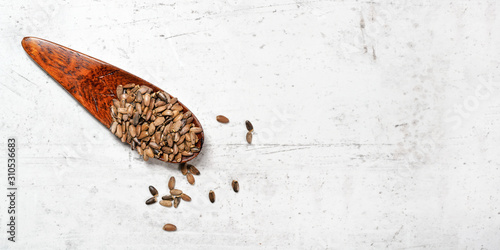 Small wooden scoop with blessed milk thistle seeds - Silybum marianum - on white stone like board, view from above, space for text right side photo