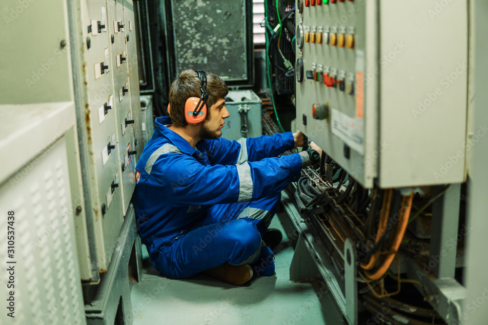 Marine engineer inspecting ship's engine or generators in engine control room ECR. Seamen's work.