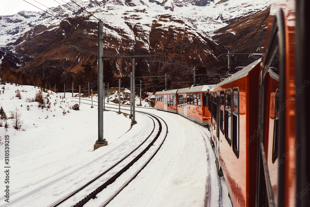 Fototapeta premium Alpine Swiss train going to the snowy Matterhorn mountain in winter. Tourists travel to mountain ski resort on railway transport from Zermatt village, Switzerland, Alps. Glacier express on the way.