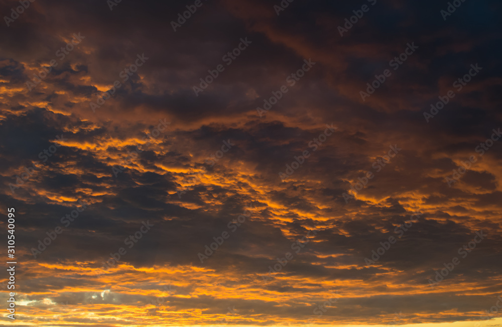 The dense relief layer of clouds is illuminated from below by the golden rays of the setting sun.