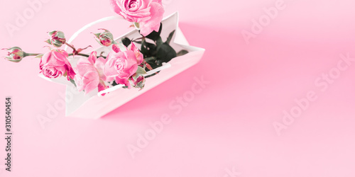 Flowers composition minimal. Pink rose flowers in white paper bag on pastel pink background. Valentines Day. Birthday, Happy Women's Day. Flat lay, top view, copy space photo