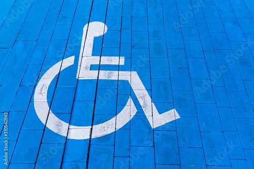 Wheelchair with information sign on brick floor, parking place for disable. White painted symbol on blue ground.