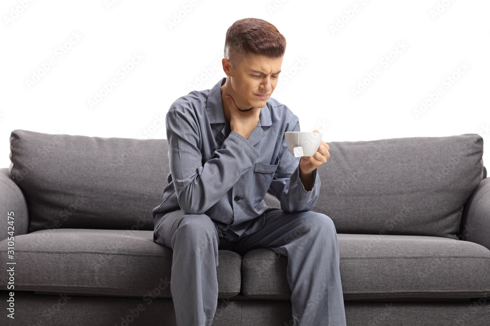 Young guy suffering from sore throat sitting on a sofa with a cup of tea Young guy suffering from sore throat sitting on a sofa with a cup of tea