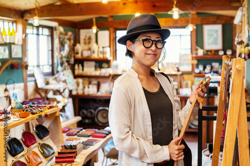 Japanese woman wearing hat and glasses standing in a leather shop, holding leather belt. photo