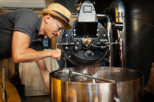 Japanese man wearing hat and glasses standing in an Eco Cafe, operating coffee roaster machine. photo