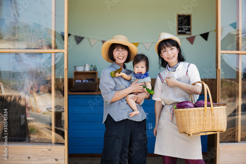 Two Japanese women and boy standing outside a farm shop, smiling at camera. photo