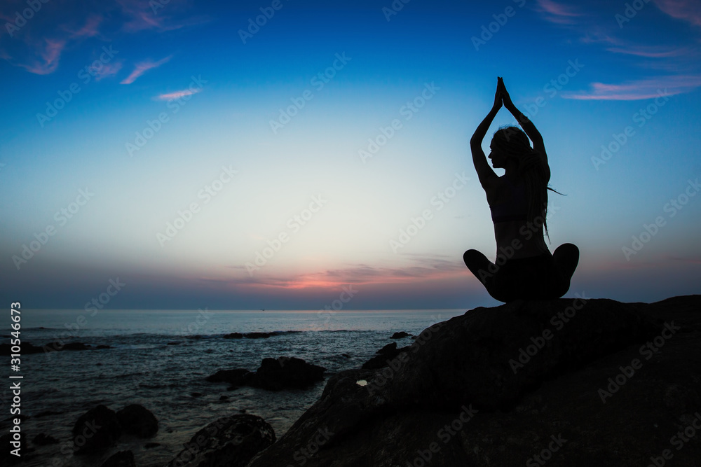 Silhouette of yoga woman in Lotus position on the shore of ocean.