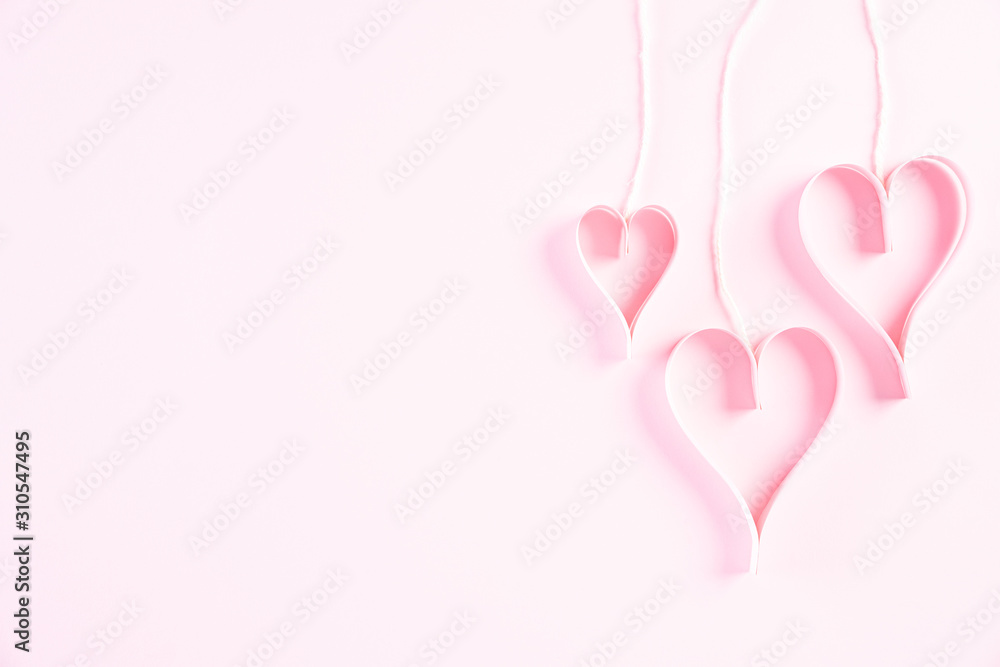 Pink paper hearts hanging on ropes on Light pink pastel paper background. Love and Valentine's day concept.