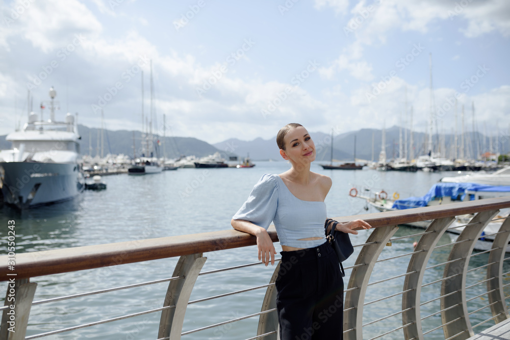 Young tourist woman on a bridge. Woman looks dreamy on the port with ships. Seascape with mountains. Summer vacation in Marmaris, Turkey. Copy space. Young tourist woman on a bridge. Woman looks dreamy on the port with ships. Seascape with mountains. Summer vacation in Marmaris, Turkey. Copy space.
