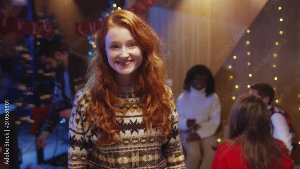 Cute pretty red-haired young woman wearing Christmas sweater staying with friends at night party. Amazing holiday ginger girl smiling cheerful celebrating magic New Year's Eve. Cute pretty red-haired young woman wearing Christmas sweater staying with friends at night party. Amazing holiday ginger girl smiling cheerful celebrating magic New Year's Eve.