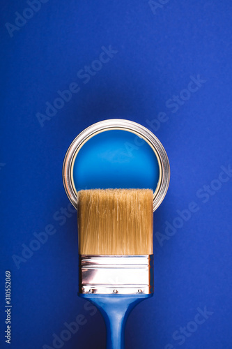 Brush on open can of blue paint on blue background. Color of the year in interior.