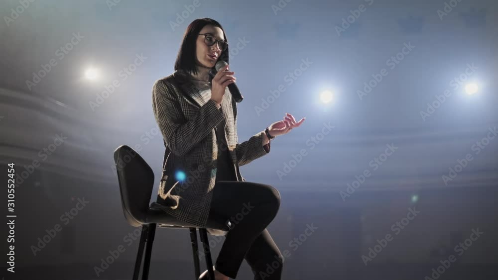 The female financial coach emotional gesturing talks from the stage with spectators at forum. Too many anonymous persons workers and students seat in large auditorium and watch workshop background The female financial coach emotional gesturing talks from the stage with spectators at forum. Too many anonymous persons workers and students seat in large auditorium and watch workshop background