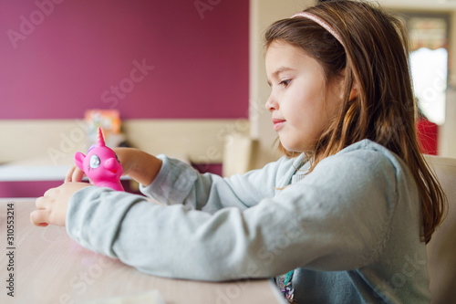 Small girl young caucasian child playing with her toy while sitting at the table in front of purple wall