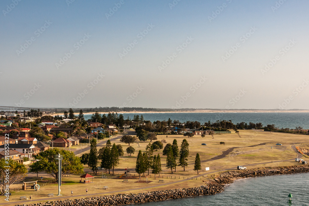 Newcastle, Australia - December 10, 2009: Looking over Stockton peninsula with its South Pacific shoreline forming a bow on the horizon under light blue to silver sky. Green foliage in front.