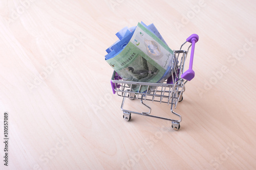 Small shopping trolley with ringgit banknotes on wooden background.