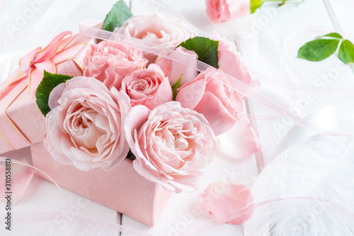 Beautiful pink flowers in gift box with ribbons closeup on white wooden table.