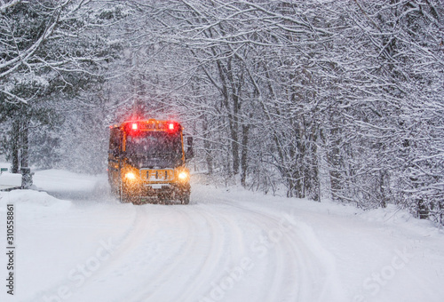 School Bus Travelling on a Snow Covered Rural Road with Stop Lights Flashing