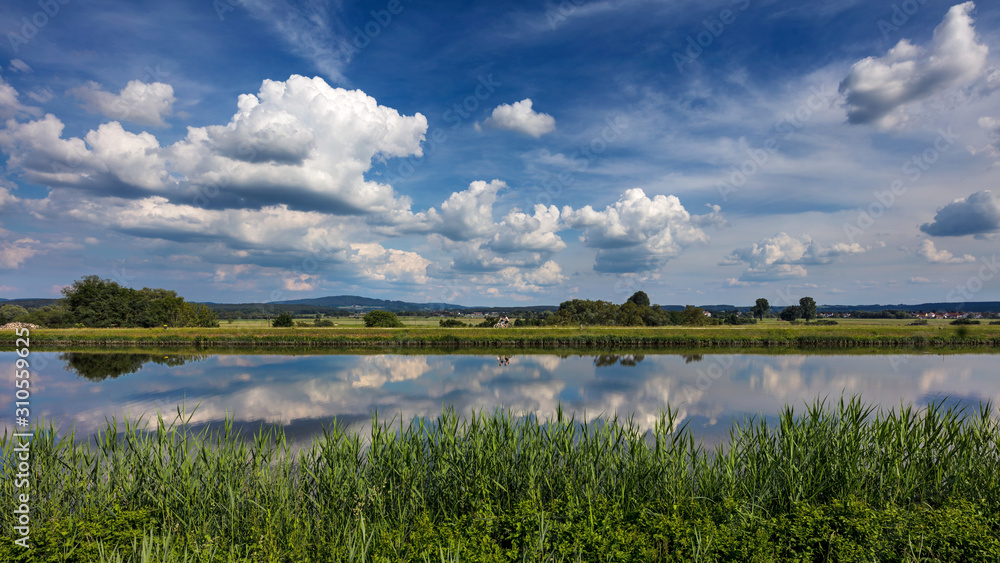 Dramatic clouds in blue sky reflect in the water of the the Rhine-Main-Danube Canal near Forchheim, Germany. 