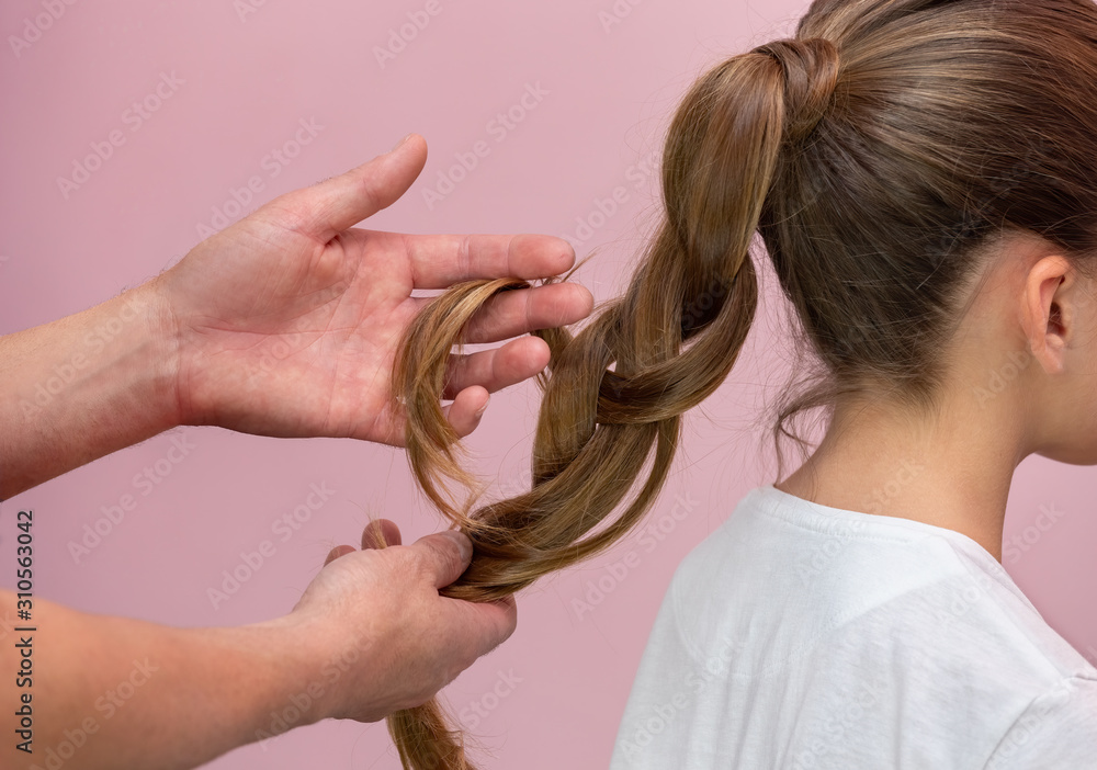 Fototapeta premium Hairdresser braiding a female child in a white shirt