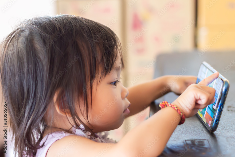 Soft​ focus.​ Portrait​ image​ of​ 1-2​ yeas​ old​ baby.​ Happy​ Asian​ child​ girl​ using and​ playing​ a​ smart Phone.​ 