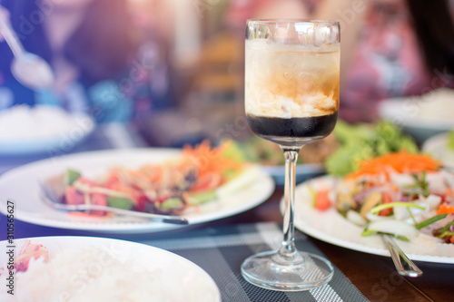 A glass of Black Russian alcoholic cocktail, liquor menu cool drink on the wooden table in the restaurant with blurred people and dish of food